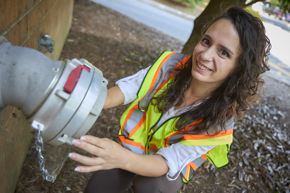 Adult female student kneeling by a water nozzle for a large hose